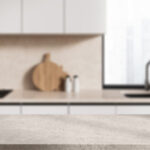 Modern kitchen with a stone countertop, blurred white cabinets, cutting boards, and a sink near a window in the background.