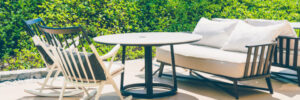 Outdoor patio with a round table, two rocking chairs, and a cushioned sofa set against a green leafy background.