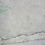 Cracked concrete pavement with a visible horizontal split near the bottom and some faded green paint in the upper left corner.