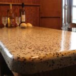 Polished terrazzo countertop with two wine bottles, two glasses, and two bread rolls in a kitchen setting.