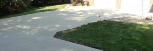 Freshly poured concrete driveway next to a patch of green grass in front of a brick house with two garage doors.