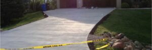 Freshly poured concrete driveway in front of a house, blocked off with caution tape to prevent entry.