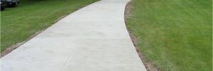 A long concrete driveway curves through a grassy yard toward a house with an open garage.